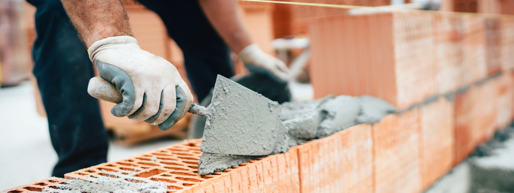 Professioneller Arbeiter beim Bau von Ziegelwänden mit Zement und Mörtel mit einem Topfmesser